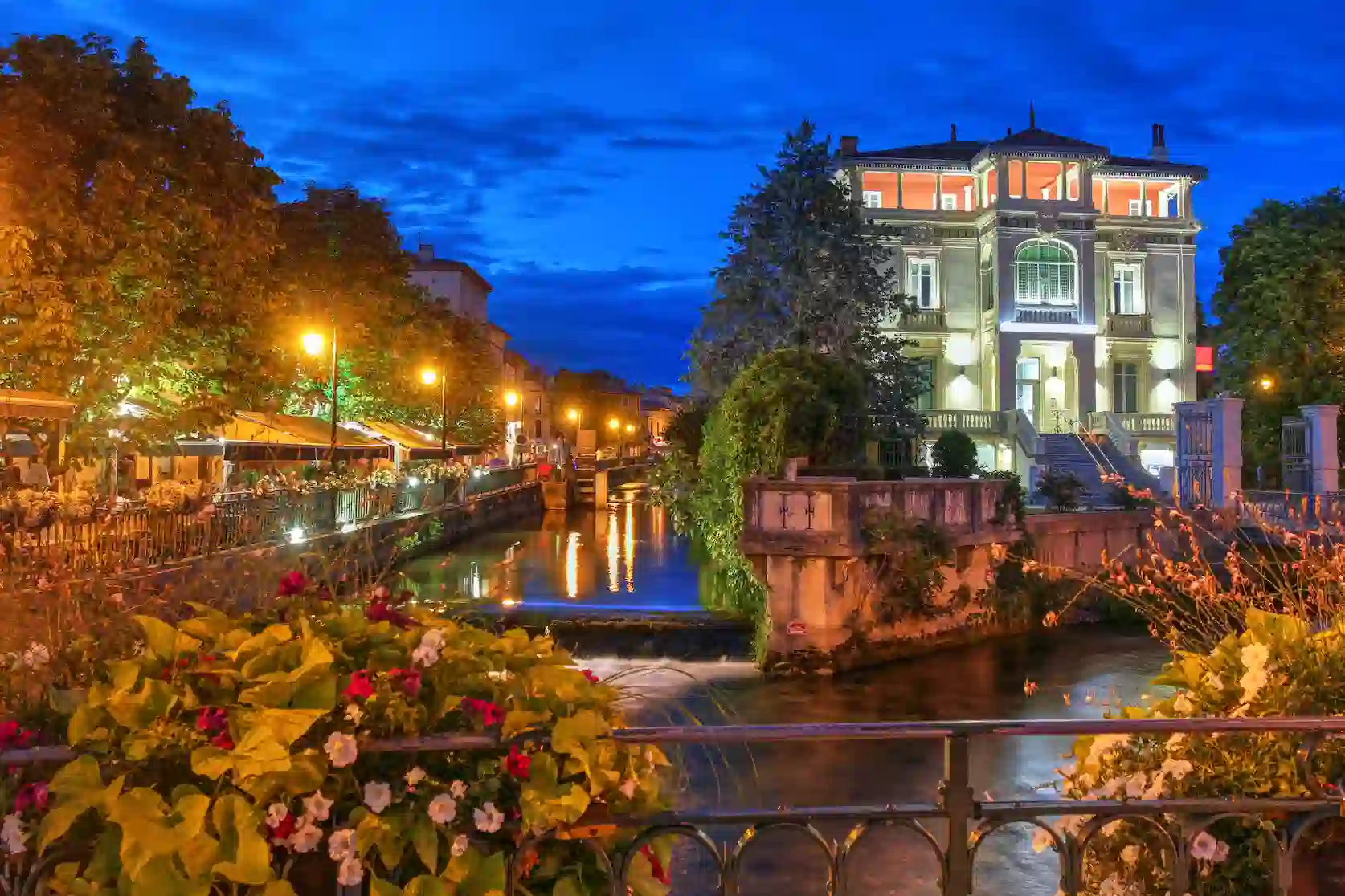 Vue nocturne de L’Isle-sur-la-Sorgue avec la rivière éclairée et ses bâtiments illuminés.