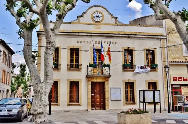 Vue de l’Hôtel de Ville de Senas, avec son horloge et ses drapeaux français et européens, entouré de la place pittoresque du village.