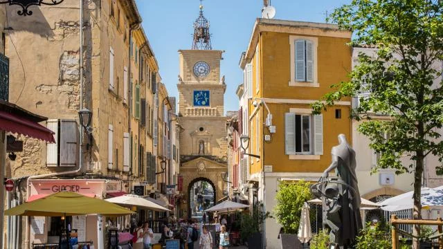 Rue de Salon-de-Provence avec l’horloge de la ville en arrière-plan, entourée de bâtiments historiques et de terrasses de cafés typiques.