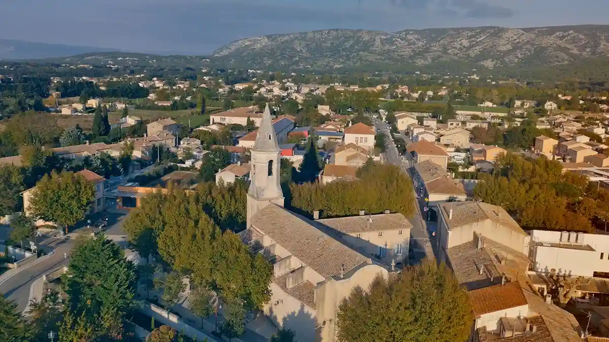 Vue aérienne de Cheval-Blanc, village pittoresque des Alpilles, avec ses maisons traditionnelles et son église, niché dans un environnement naturel verdoyant.